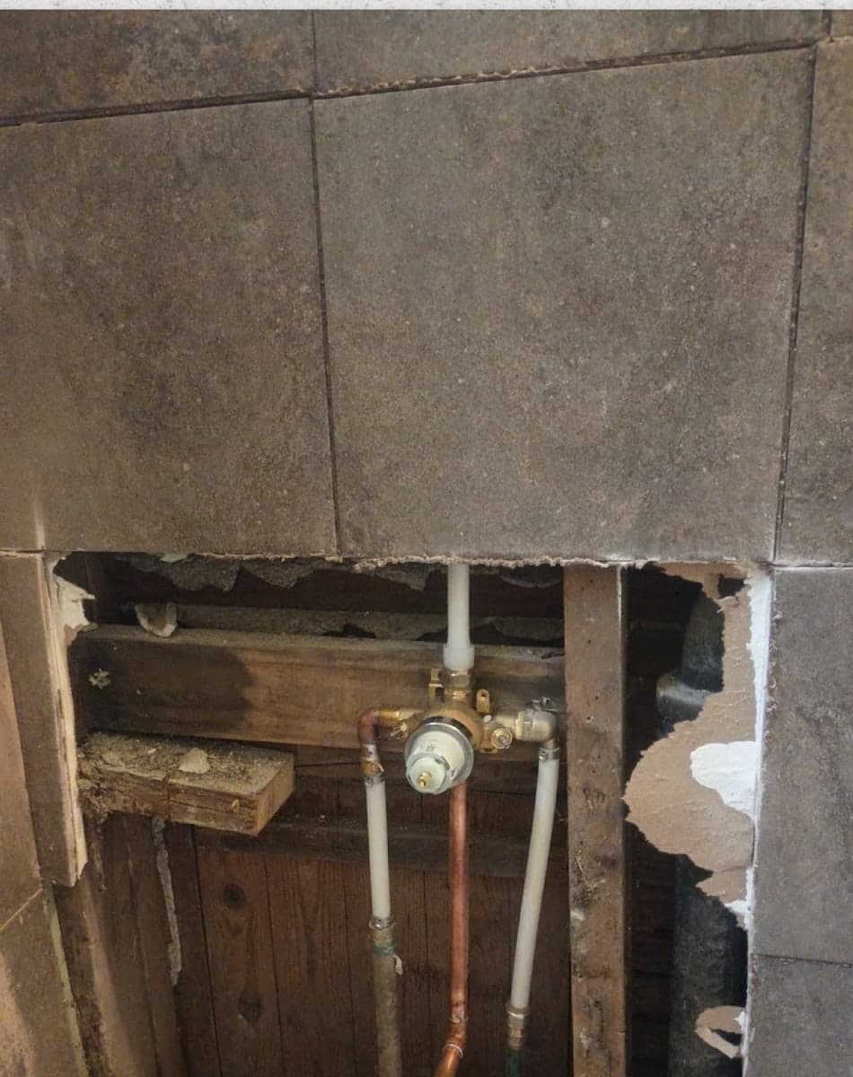 Bathroom tile wall cut open to expose the shower valve and plumbing before repair by Drywall & Remodeling ETC. in Memphis, TN